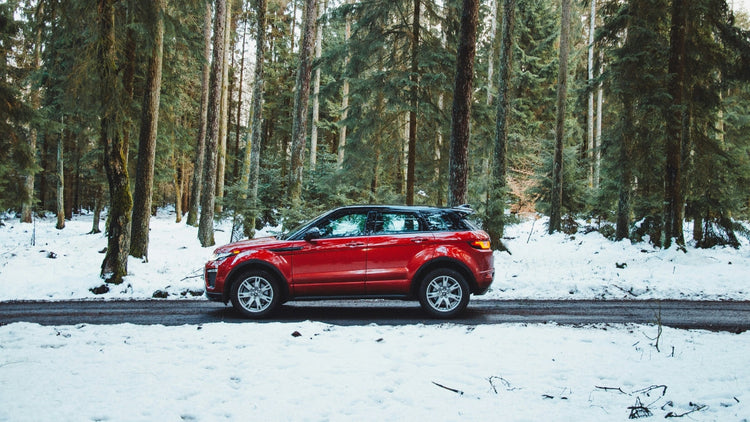 Red SUV on a snowy winter road, demonstrating the importance of reliable car battery performance in cold weather.